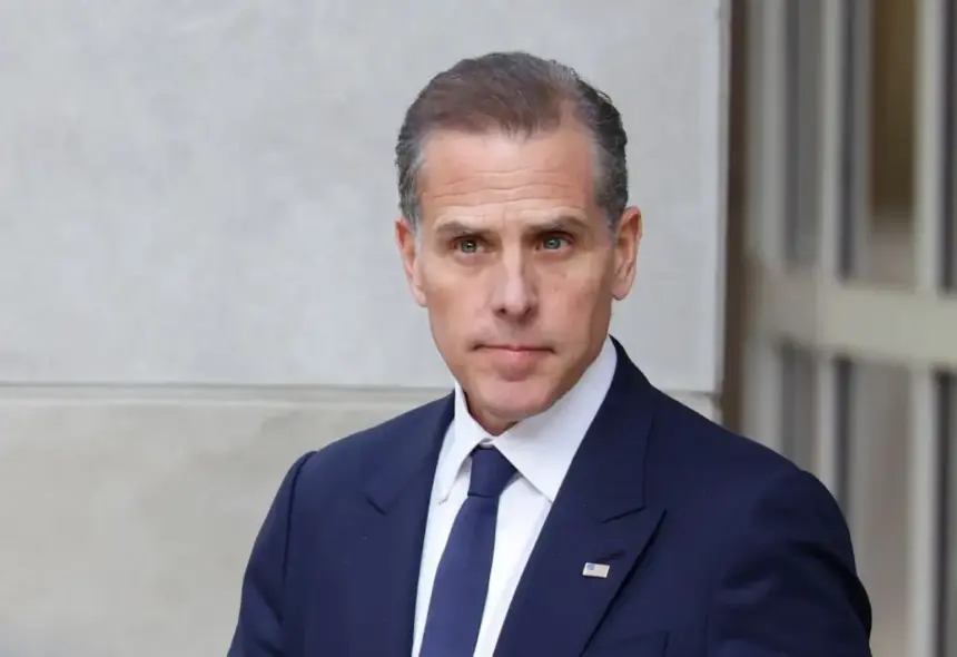 Portrait of Hunter Biden in a suit, standing thoughtfully with a neutral background.
