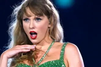 Portrait of Taylor Swift performing on stage during her Eras Tour, wearing a sparkling bodysuit and holding a microphone.