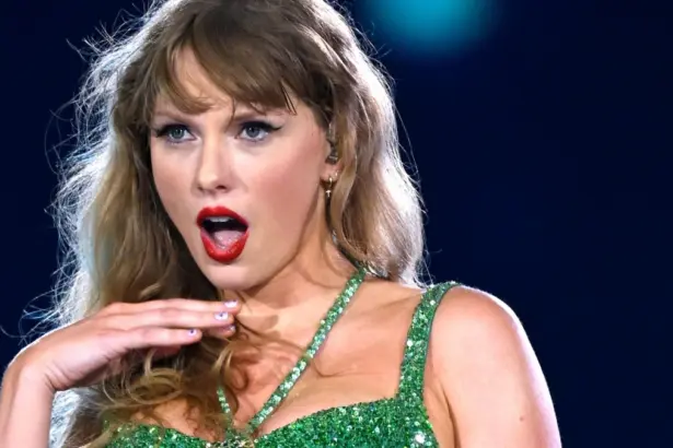 Portrait of Taylor Swift performing on stage during her Eras Tour, wearing a sparkling bodysuit and holding a microphone.