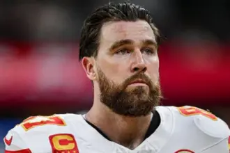 Travis Kelce celebrating on the field with the Kansas City Chiefs, holding a football.
