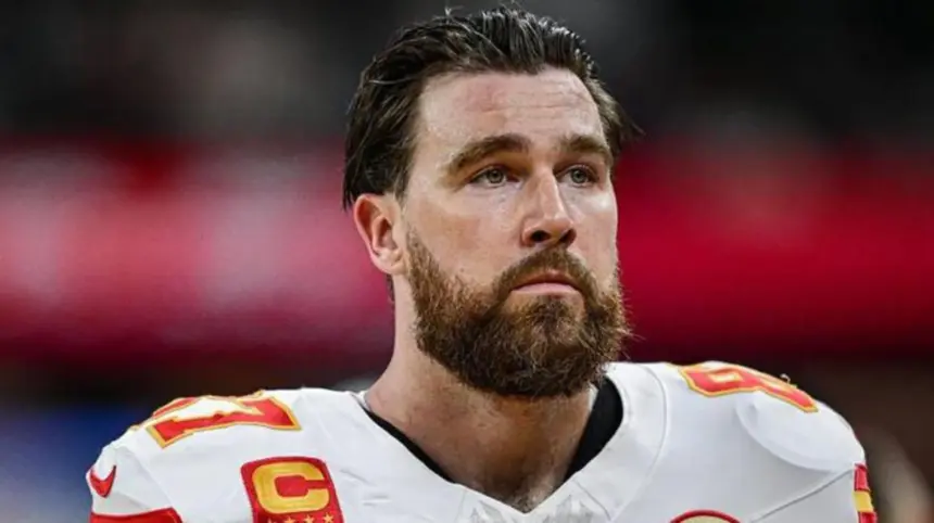 Travis Kelce celebrating on the field with the Kansas City Chiefs, holding a football.