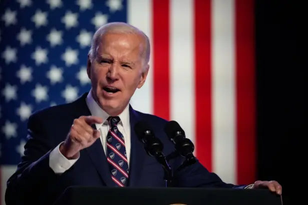 Portrait of Joe Biden smiling in a suit, standing in front of the American flag.